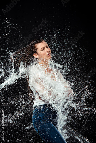 side view of woman in white shirt and jeans swilled with water isolated on black
