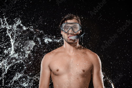 portrait of shirtless man in swimming mask with snorkel swilled with water isolated on black