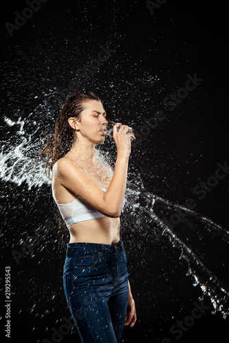 side view of woman swilled with water while drinking water from glass isolated on black