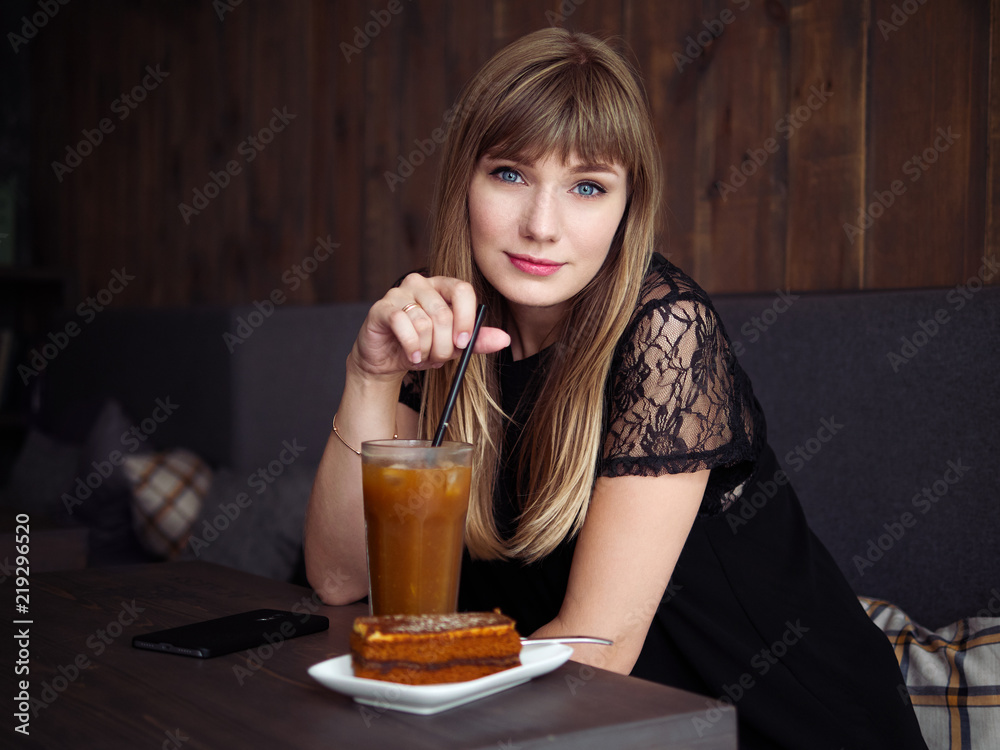 Charming young woman with beautiful smile enjoying orange juice frappe in cozy coffee shop relaxing during free time Charming young woman with beautiful smile enjoying orange juice frappe in cozy coffee shop relaxing during free time