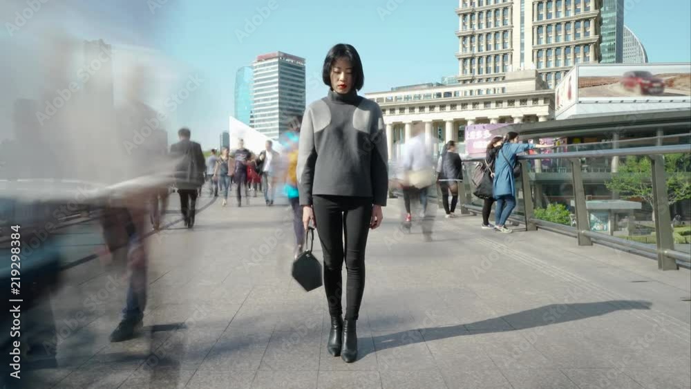 Timelapse of woman standing on crowded walkway. Time lapse of girl standing still while a blur of fast moving people move around her; frozen in time, crowds whiz past.