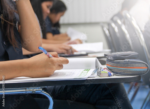 Hands university student holding pen writing /calculator doing examination / study or quiz, test from teacher or in large lecture room, students in uniform attending exam classroom educational school.
