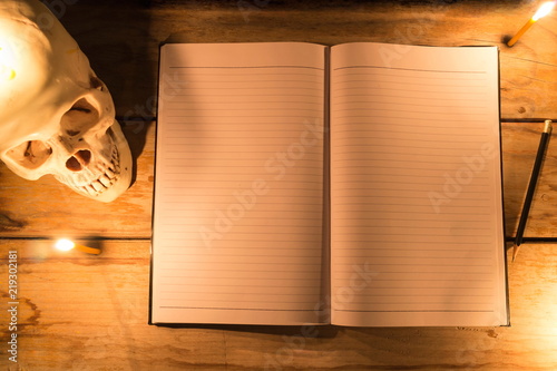 Human skull with candle light and notebook with pencil on wooden table, Decorated for Halloween Theme with copy space.