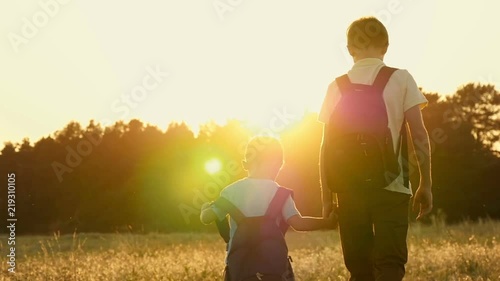 Two brother of a tourist, walking with backpacks, holding on to the background at sunset in slow motion. Happy children are walking in nature photo