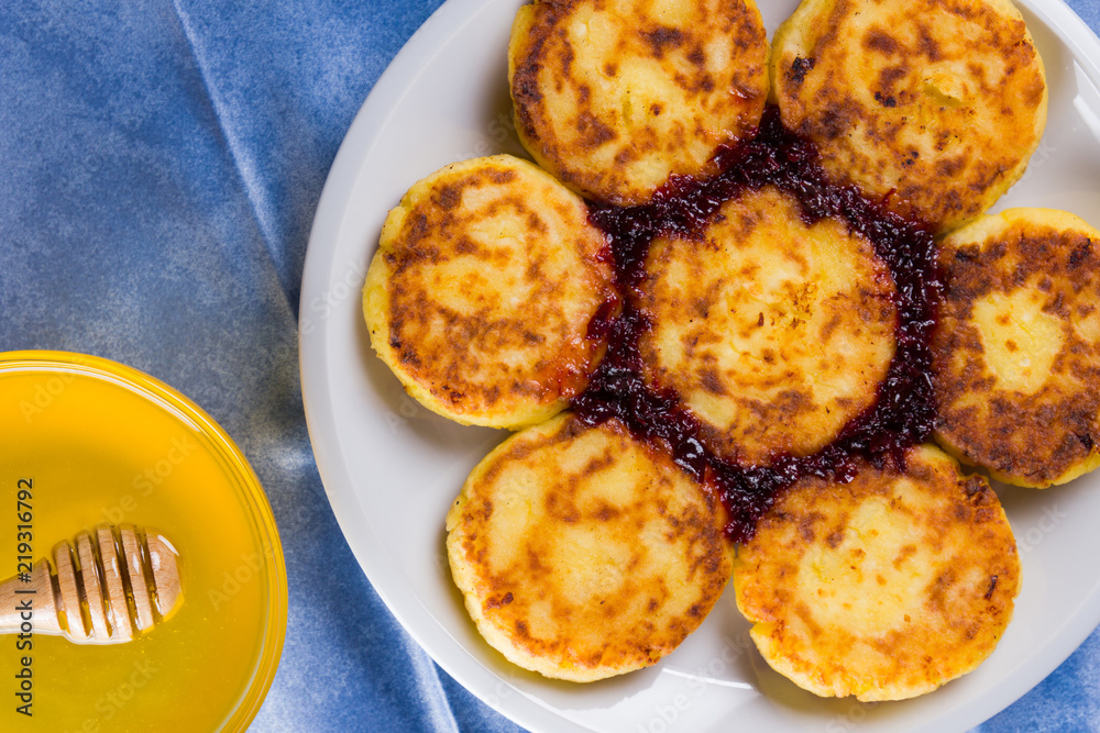 Cottage cheese pancakes on blue napkin. Traditional Ukrainian dish - syrniki with jam on a wooden background. Pancakes with cottage cheese on a white plate with honey