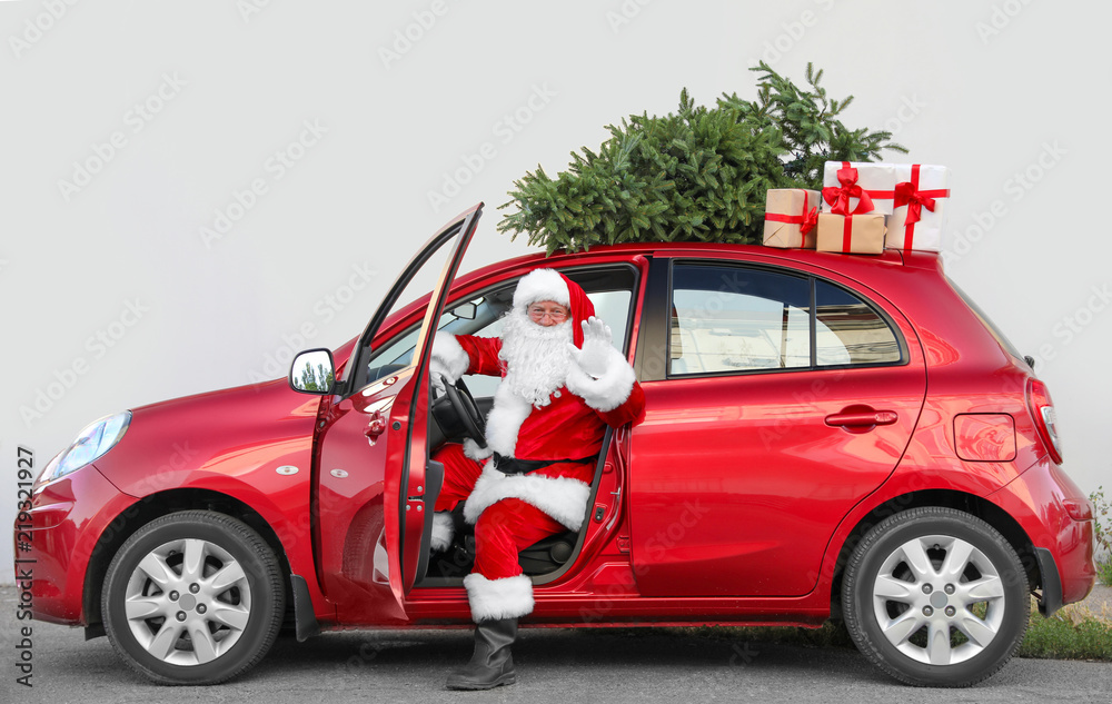 Naklejka premium Authentic Santa Claus in car with gift boxes and Christmas tree, view from outside