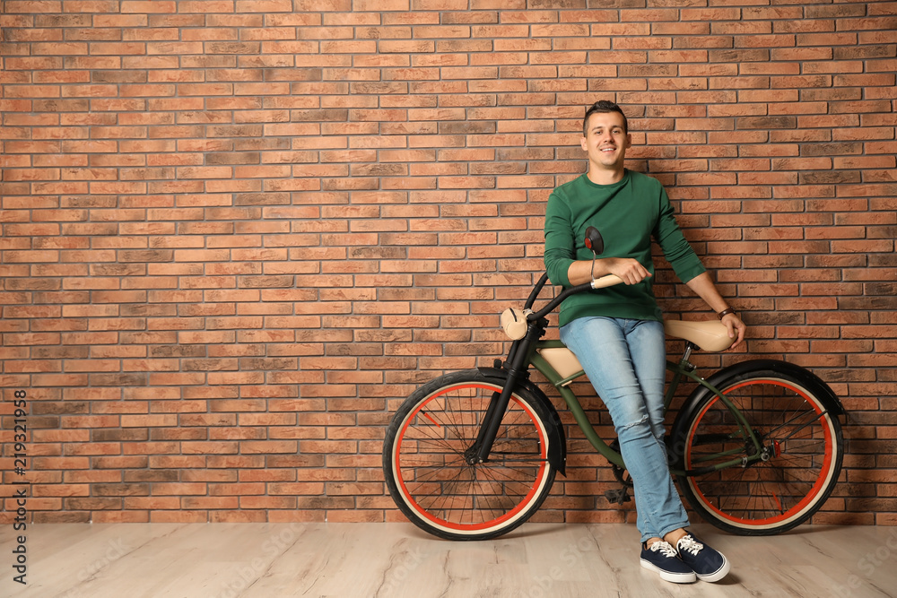 Fototapeta premium Portrait of handsome young man with bicycle near brick wall