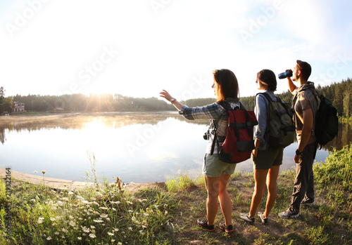 Fotografi Young friends on shore of beautiful lake, wide-angle lens effect