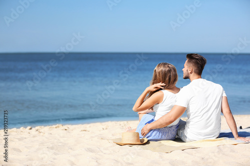Happy young couple sitting together at beach on sunny day