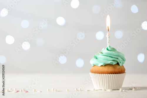 Delicious birthday cupcake with burning candle and space for text on blurred lights background photo