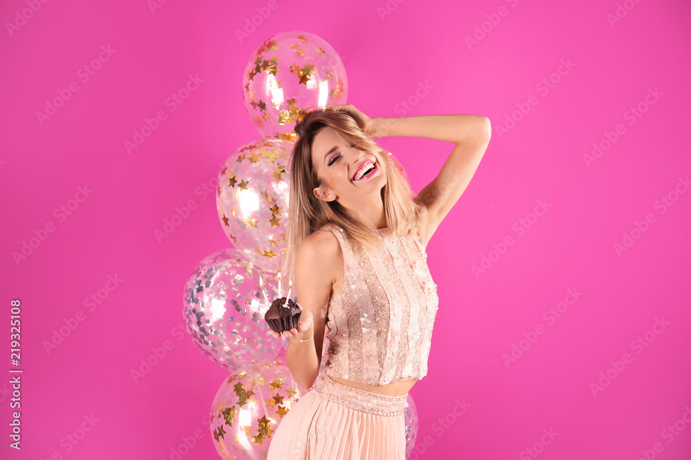 Young woman with birthday muffin and air balloons on color background