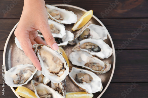 Top view of woman with fresh oyster over plate, focus on hand