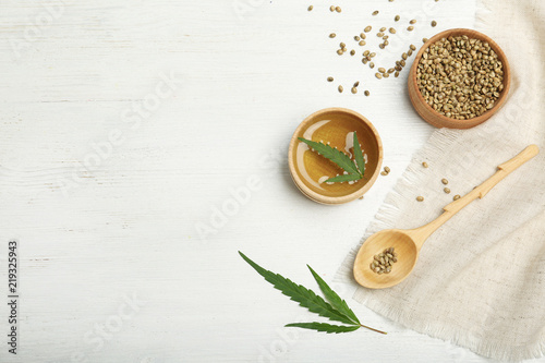 Hemp oil, seeds and space for text on white wooden background, flat lay