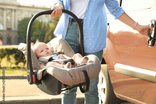 Mother holding child safety seat with baby near car outdoors