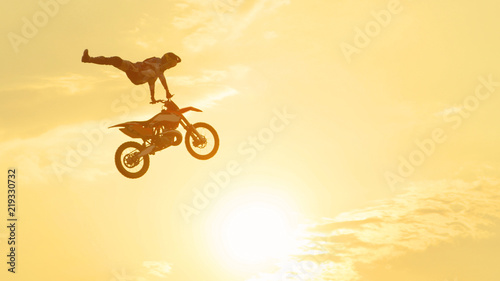 Pro freestyle motocross biker jumping extreme trick over sunset sky