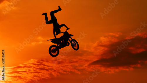 Extreme pro motocross biker jumping freestyle trick over the sun