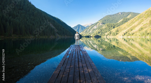 businessman in a white suit is standing on a pier by the lake