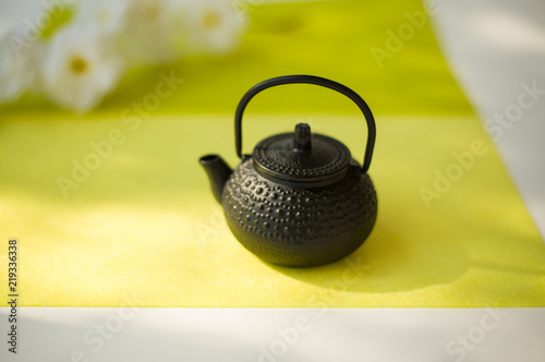 side view of cast iron teapot on light yellow background with white flowers