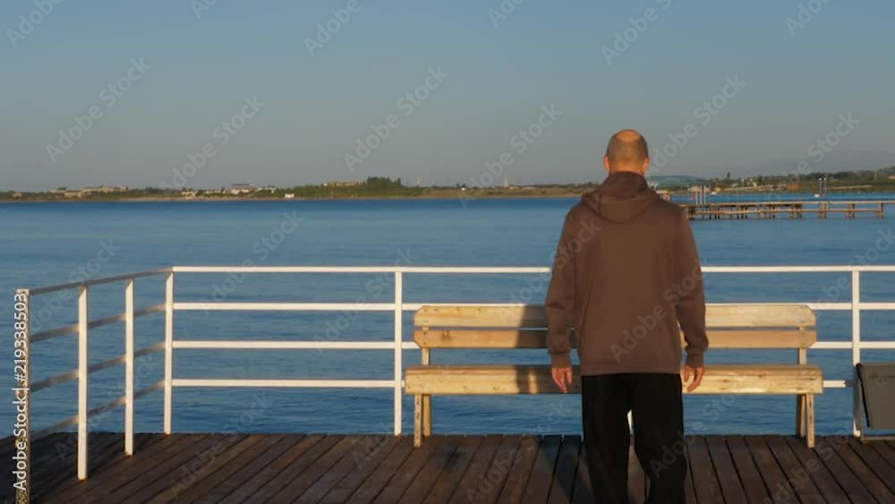 Adult man walking on pier blue lake water and looking on landscape back view Adult man walking on pier blue lake water and looking on landscape back view