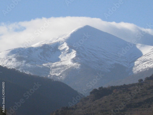 Pico de montaña nevada, con sierra delante y nube detrás photo