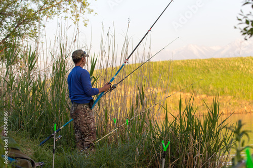 Fisherman with a fishing rod on the river bank. A fisherman is fishing. Fish, rotating coil. - The concept of rural recreation. Article about fishing.
