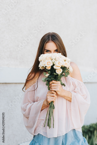 Happy beautiful woman with soft white roses, wearing blush cold shoulder blouse