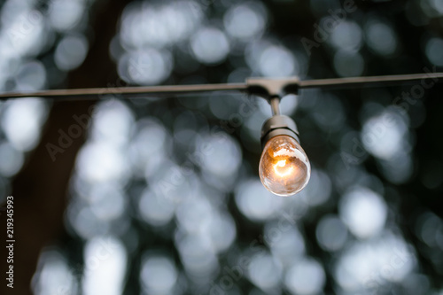 A single glowing light bulb hangs with bokeh in the background