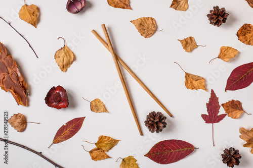 Autumn background: autumn leaves and asian chopsticks hold pinecone. Top view, flat lay.