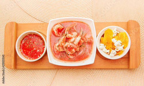 Above view of delicious shrimp cebiche in rectangular white bowl served with chifles and red spicy sauce over a wooden structure in table background photo