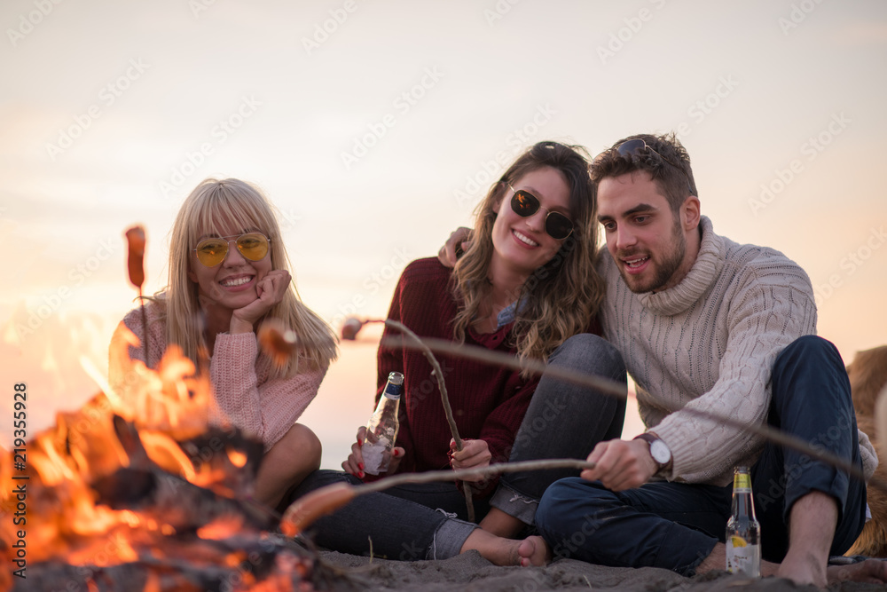 Fototapeta premium Group Of Young Friends Sitting By The Fire at beach