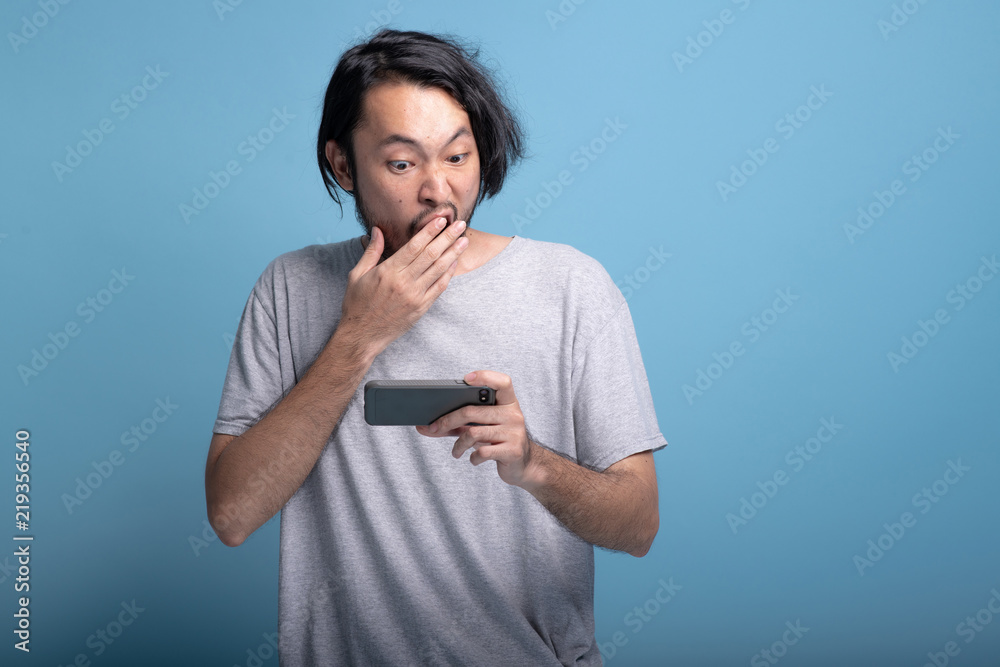 Excited Young bearded man playing mobile games in blue background. Excited Young bearded man playing mobile games in blue background.