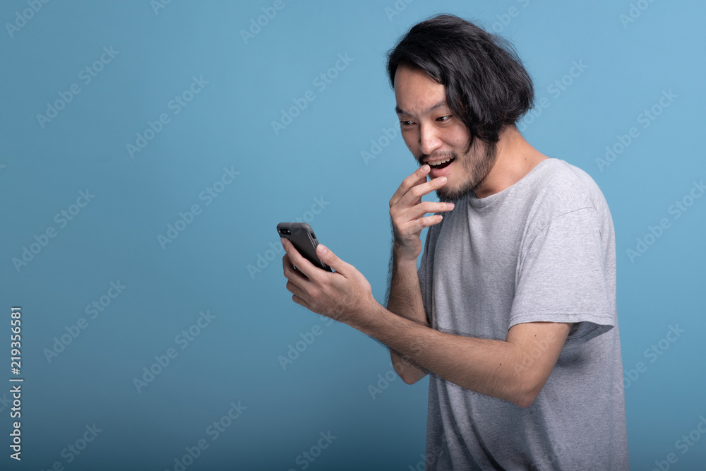 Excited Young bearded man looking at mobile message in blue background.