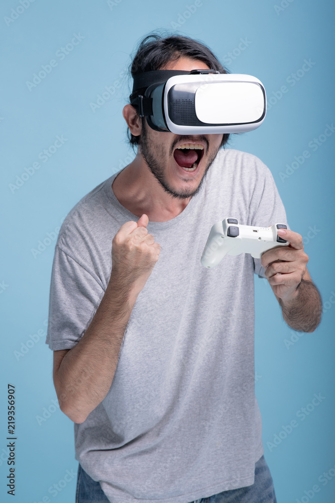 Young bearded man playing VR game in blue background. Young bearded man playing VR game in blue background.