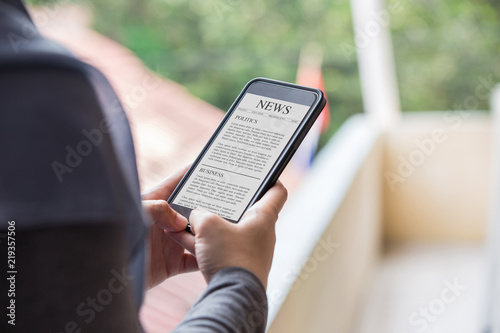 News article concept on phone screen. Woman hand holding smartphone reading news article on screen.