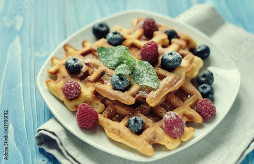 Belgian waffles with blueberries, raspberries and powdered sugar on wooden table.