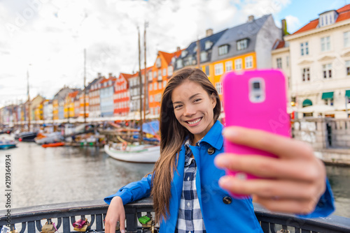 Photography Selfie tourist girl taking photo with phone at Copenhagen Nyhavn, famous Europe tourism attraction
