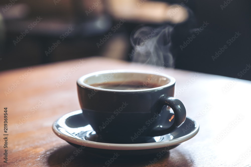 Fototapeta Closeup image of a blue cups of hot coffee with smoke on vintage wooden table in cafe
