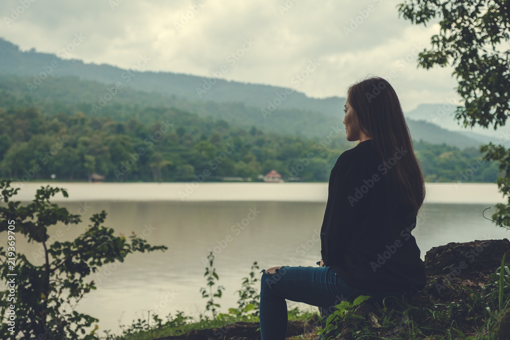 Closeup image of an asian woman sitting alone by the river with sky and mountain background Closeup image of an asian woman sitting alone by the river with sky and mountain background