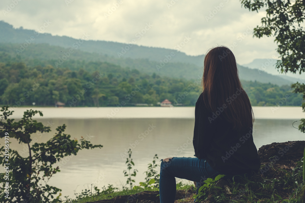 Closeup image of an asian woman sitting alone by the river with sky and mountain background