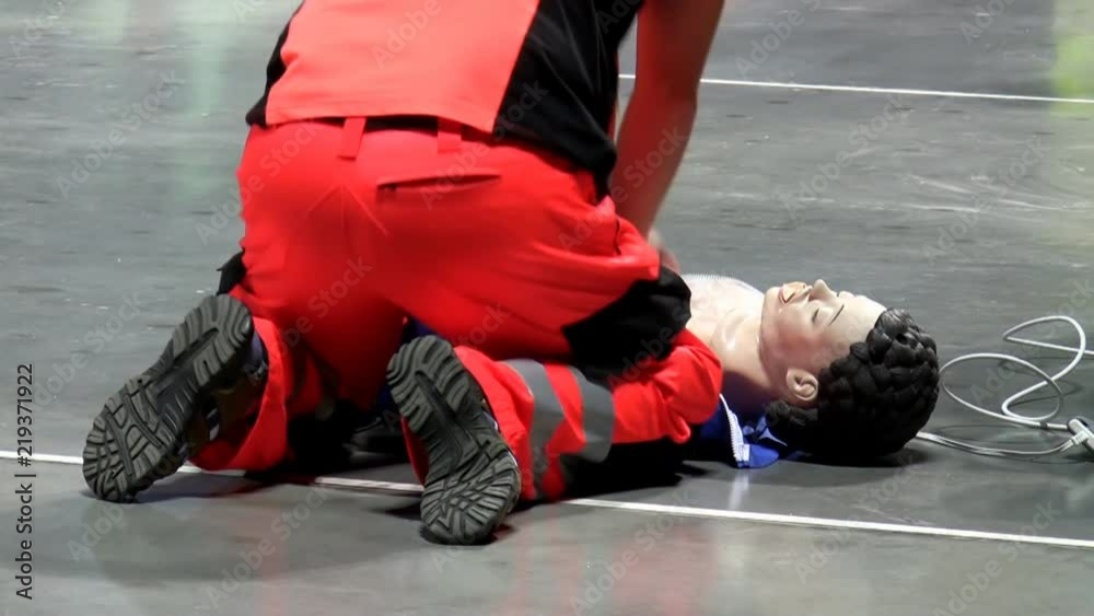 Man in red paramedic uniform on the floor doing chest compression on CPR dummy on the floor, rear view