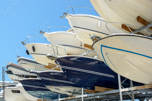 Foto View from below of the hulls of motorboats racked one above another on two levels in a dry rack boat storage facility against blue sky