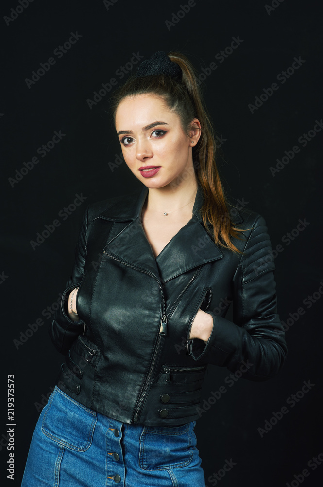 Studio portrait of a young beautiful girl in a stylish leather jacket, smiling girl on a dark background Studio portrait of a young beautiful girl in a stylish leather jacket, smiling girl on a dark background