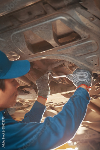Automobile mechanic wearing gloves when tightening nuts on car bottom