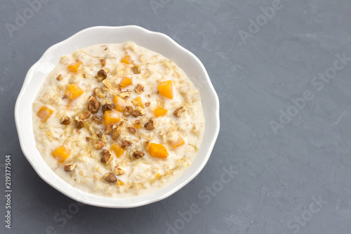 Pumpkin oatmeal with honey and nuts, milk in a milkman, walnuts on a gray background. healthy delicious homemade breakfast. free space