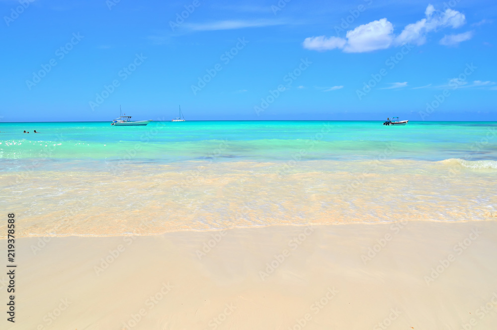 coast of the Caribbean Sea, white sand, beautiful azure water of the sea, boats and boats on the horizon, blue sky covered with light white clouds