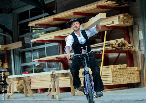 Zimmermann mit Balken auf der Schulter fährt Fahrrad vor Holzlager photo