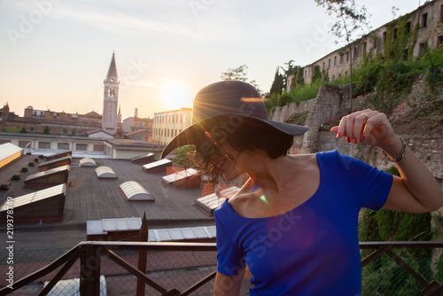 Close-up of young woman's face with wide-brimmed black hat. Outdoor against the sun at sunset on a city (Verona, Italy). Outdoor atmosphere with warm colors. at sunset 