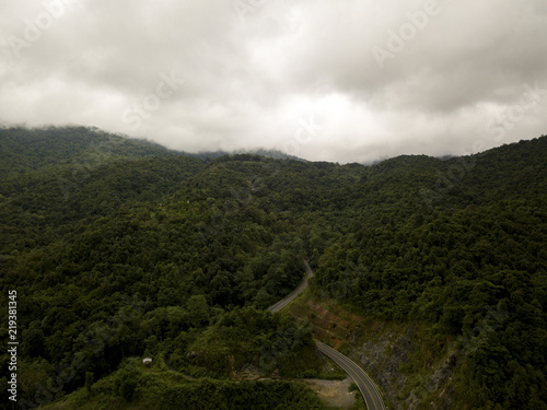 Aerial view of countryside road passing through the lush greenery and foliage tropical rain forest mountain landscape in the Northern Thailand