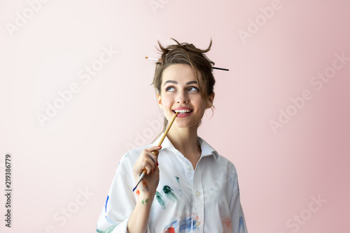 Beautiful young woman biting brush in happy dreams