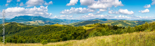 panorama of a beautiful landscape. grassy meadows and forested hills in early autumn. mountain ridge in the distance beneath a blue sky with clouds